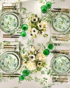 a table set with green and white plates, silverware and flowers on the tablecloth