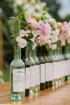 several bottles with flowers in them are lined up on a wooden table and labeled with labels