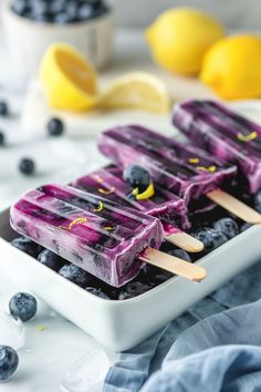 two popsicles with blueberries and lemons on them sitting in a white dish