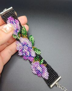 a hand holding a beaded watch strap with beads on it's side and a chain attached to the clasp