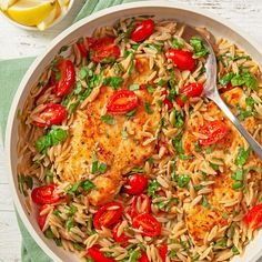 a white bowl filled with pasta and meat covered in tomatoes, green herbs and lemon wedges