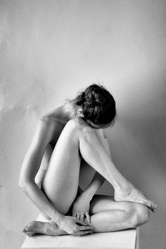 black and white photograph of a naked woman sitting on top of a table with her legs crossed