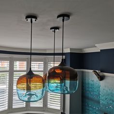 three glass pendant lights hanging from the ceiling in a room with blue walls and windows