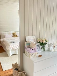 a white dresser sitting next to a bed with flowers on top of it in a bedroom