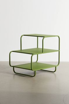 three tiered green shelf sitting on top of a cement floor next to a white wall