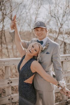 a man and woman in formal wear posing for a photo on a wooden bridge with trees in the background