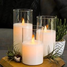 three white candles sitting on top of a wooden tray