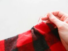 someone is sewing on a red and black checkered blanket with their hand over the edge