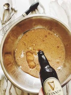 a bottle of beer is being poured into a metal bowl