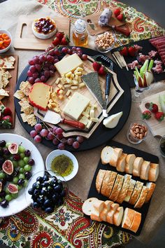 an assortment of cheeses, crackers and grapes on a table with other foods