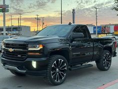 a black chevrolet truck parked in a parking lot at sunset with the sun setting behind it