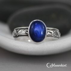 This striking Blue Sapphire Ring features a 10 mm x 8 mm oval cabochon of lab grown Blue Sapphire that has been securely set in a fine silver bezel. Traditionally, people attributed to Blue Sapphire the power to bring harmony between lovers as well as peace between adversaries. We are happy to create this beautiful ring for you in a variety of ring sizes, finish options, or in any of the stone choices shown in the images above. The band of this Sterling Silver ring features an Art Deco inspired Celestial Oval Cabochon Rings, Blue Sapphire Ring Oval Cabochon, Gift Sapphire Oval Cabochon Ring With Polished Finish, Sapphire Cabochon Rings For Gifts, Sapphire Jewelry With Oval Cabochon For Gift, Celestial Blue Cabochon Ring, Spiritual Sapphire Oval Rings, Sapphire Cabochon Ring As A Gift, Blue Polished Moonstone Ring Gift