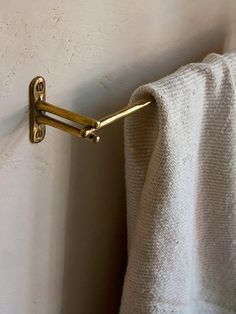 a towel hanging on the side of a white wall next to a metal hook with gold handles