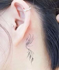 a woman's behind the ear has a small bird tattoo on it