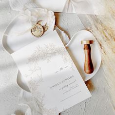 the wedding stationery is laid out on a plate and next to a wooden ring