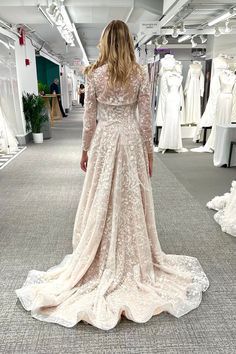 a woman in a wedding dress is looking at dresses on mannequins behind her