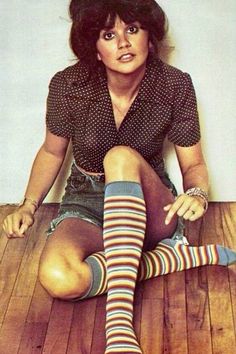 a woman sitting on top of a wooden floor wearing striped socks and knee high socks