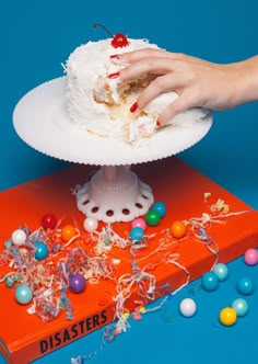 a hand reaching for a piece of cake on top of an orange book with colorful candies around it