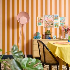 a dining room with yellow table cloths and pink floor lamp in front of striped wallpaper