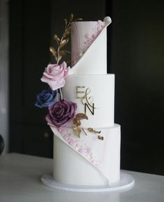 a three tiered white cake with purple and blue flowers on the top, sitting on a table