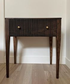 a small wooden table with two drawers on it's sides, against a white wall