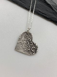 This floral silver heart necklace has been entirely handmade using .999 fine silver. It has been cut from fine silver precious metal clay, textured, fired and oxidized. The pendant hangs from a sterling silver diamond cut cable chain. This fine silver pendant features an embossed lovely rose textured print. Pendant size: approximately 3/4 x 3/4 inches Chain length: adjustable at 16 and 18 inches can also be customized to whatever length needed The necklace is sent in a gift box. This jewelry can Unique Etched Sterling Silver Necklace, Etched Sterling Silver Necklace Gift, Etched Sterling Silver Necklace For Gift, Sterling Silver Etched Necklace For Gift, Silver Etched Necklace With Flower Pendant, Etched Sterling Silver Necklaces, Sterling Silver Etched Jewelry For Gifts, Etched Sterling Silver Jewelry As Gift, Sterling Silver Etched Jewelry As Gift