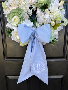 a wreath on the front door decorated with white flowers and blue ribbon is displayed in front of a black door