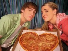 a man and woman posing with a heart shaped pizza