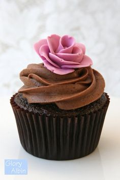 a cupcake with chocolate frosting and a pink flower on top is sitting on a white surface