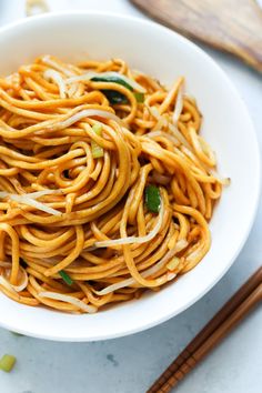 a white bowl filled with noodles next to chopsticks