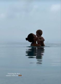 a woman and child are kissing in the middle of an ocean with blue sky behind them