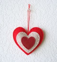 a red and white heart ornament hanging from a string on the side of a wall