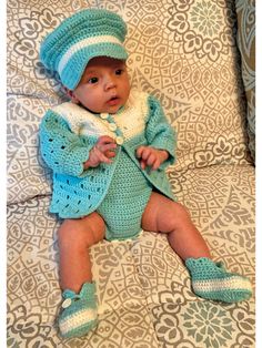 a baby wearing a blue crochet outfit and hat laying on top of a couch