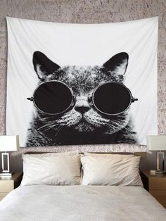 a black and white photo of a cat with sunglasses on it's face hanging over a bed