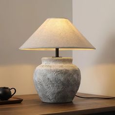 a table lamp sitting on top of a wooden table next to a teapot and cup