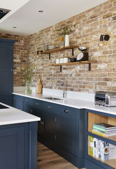 a brick wall in a kitchen with blue cabinets and white counter tops, along with open shelving