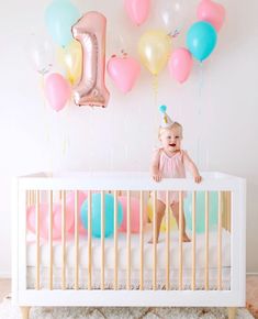 a baby is sitting in her crib with balloons