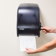 a person holding a roll of toilet paper in front of a black hand dryer