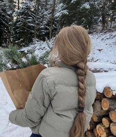 a girl with long hair holding a brown paper bag in her hand while walking through the snow