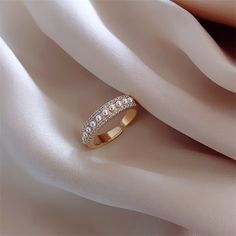 a gold ring with three rows of diamonds on top of white satin material and the words golicc written in chinese