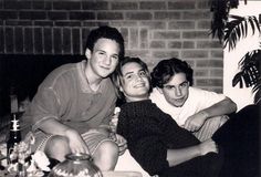 three young men sitting next to each other in front of a brick wall and fireplace