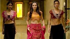 three women dressed in belly - baring outfits walking down a hall together, one wearing a red and yellow top