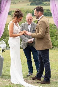 a bride and groom exchanging their wedding vows under an arch with purple draping