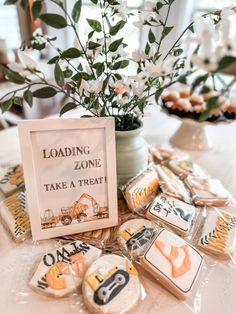 some cookies are sitting on a table next to a vase with flowers and a sign that says loading zone take a treat