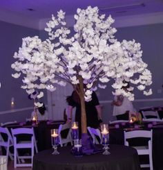 a tree with white flowers and candles in front of a black table cloth covered banquet room