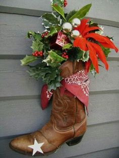 a cowboy boot with christmas decorations hanging on the side of a house, next to a planter