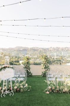 an outdoor ceremony setup with white chairs and floral arrangements on the grass, lights strung above