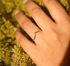 a person's hand with a ring on top of some green plants and grass