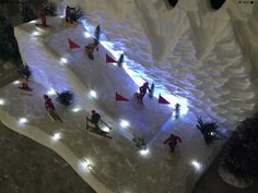 people are skiing down an artificial snow covered slope with lights on the sides and trees in the middle