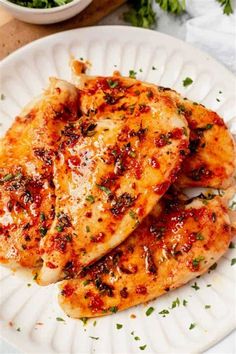 two pieces of chicken on a white plate with parsley sprinkled around it